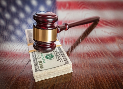 A wooden judge's gavel rests on stack of money.