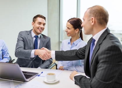 Business people are shaking hands at a table, with a laptop and coffee.