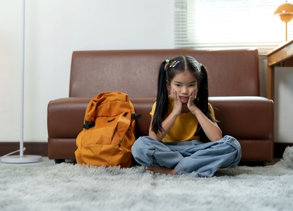 A young girl sits slumped against the couch, looking sad.