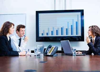 Three people in business attire are seated around a conference table.