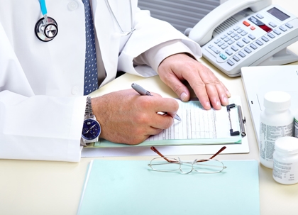 A doctor in a white coat is writing on a clipboard.