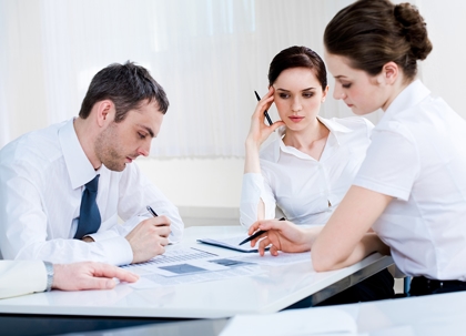 A woman is talking to a couple, likely discussing documents at a table.