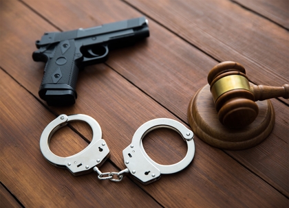 A handgun and handcuffs are next to a judge's gavel.