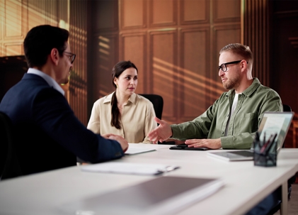 A couple sits at a desk with a person, likely a worker, looking at a computer screen.