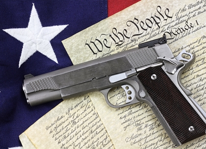 A handgun rests on a US Constitution document, with a US flag in the background.