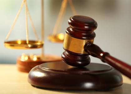 A wooden gavel on a stand, with gold-colored scales of justice in the background.