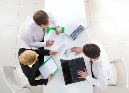 Three people, possibly a couple and a financial advisor, are seated around a laptop and paperwork.