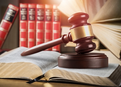 A wooden gavel rests on a dark stand and a law book