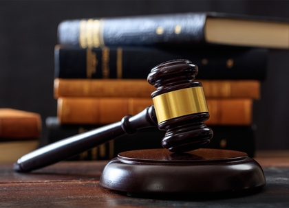 A dark-red wooden gavel rests on a stand, with many books in the background.