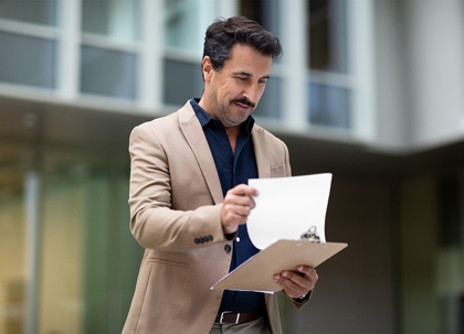 A man in a light brown suit is holding papers in a tan envelope.