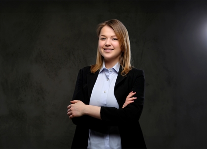 A woman in a dark suit and light shirt is smiling.