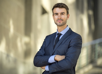 A man in a dark suit, tie, and glasses, smiling.