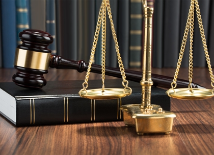 A wooden gavel, gold scales, and a law book sit on a table.