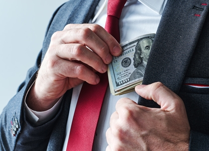 A man in a suit is putting money into his jacket pocket.