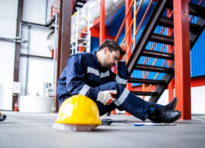 A man in work clothes is sitting on the ground, appearing distressed and injured.