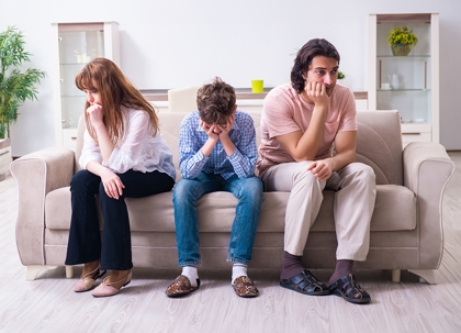 A woman and man are arguing, a girl sits between them looking sad. They are outdoors.