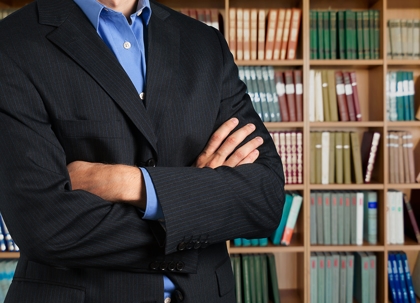 A person in a suit stands before a bookshelf filled with law books.