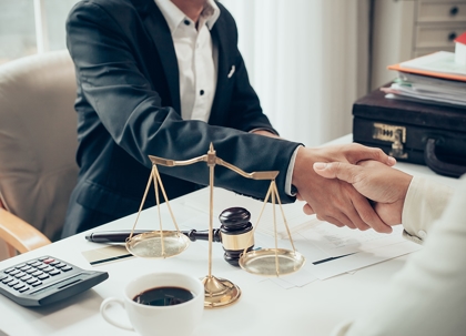 Two people in business suits are shaking hands at a table.