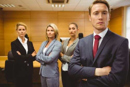 Four people in business suits, arms crossed, in a courtroom setting.