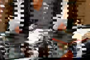 a person holding a document on their right hand and flipping the page of a thick book with their left hand