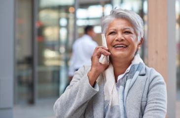 A happy older woman is talking on a cell phone outdoors.