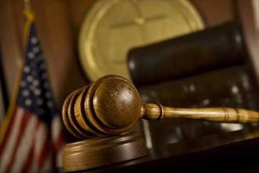 A wooden gavel rests on a stand, with an American flag and official seal in the background.
